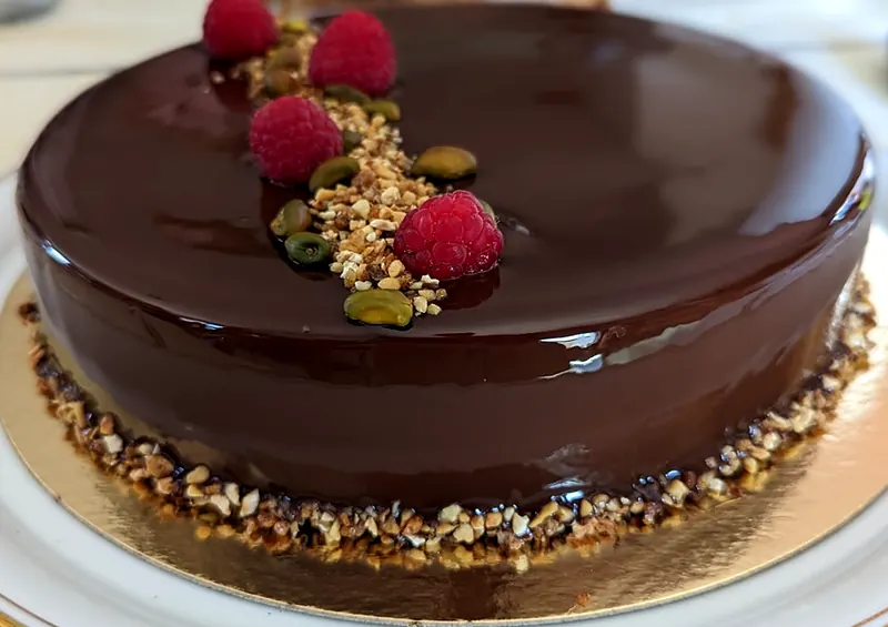 Entremets au glaçage chocolat miroir, framboises fraîches et pistaches